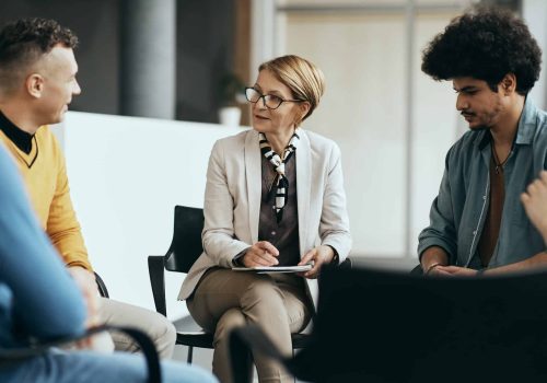 Mature therapist talking to participants of group therapy at mental health center.