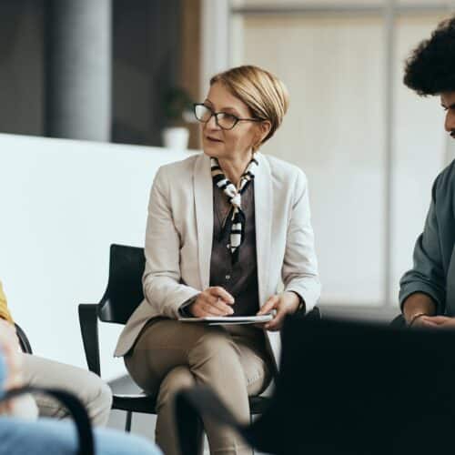 Mature therapist talking to participants of group therapy at mental health center.